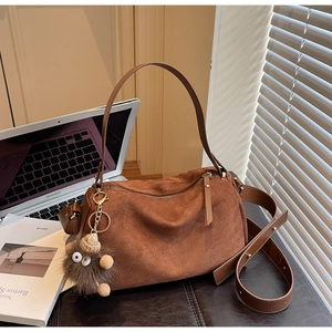 Detail of brown faux suede shoulder bag with zipper and plush doll pendant on desk