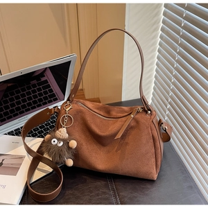 Detailed view of brown matte suede Boston bag with gold hardware and plush charm on a desk
