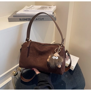 Detail of dark brown suede Boston bag featuring a playful fuzzy monster charm and leather strap
