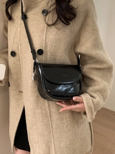 Glossy black saddle bag with peanut pendant and thin strap on a beige wool coat