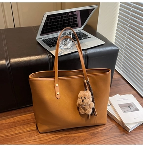 Braune Shopper-Tasche aus Leder mit Plüschbär-Anhänger auf warmem Holzboden im Detail