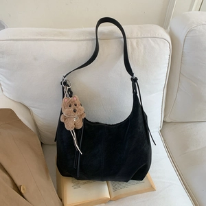 Detail of a black matte hobo bag with a plush bear charm on a cozy lifestyle background