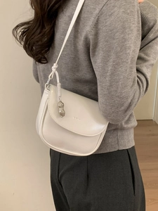 White glossy saddle bag with peanut pendant worn by model over shoulder