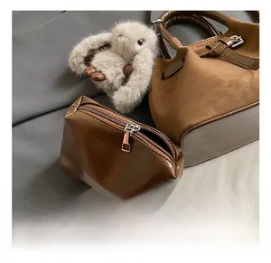 Detail of a brown tote bag with metal buckle strap and a plush bunny charm on a soft background