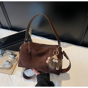 Detail of dark brown matte suede pillow bag with plush charm and adjustable strap