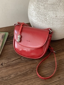 Chic red faux leather saddle bag with silver peanut charm on vintage wood surface