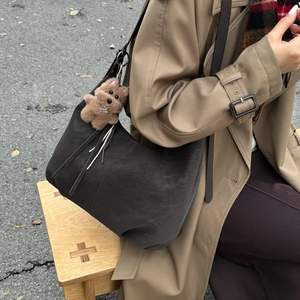 Detail of a large brown suede hobo bag with a plush bear pendant on a model in autumn wear