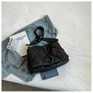 Flat lay of black quilted PU leather shoulder bag with adjustable strap on white fabric