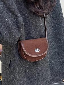 Brown suede saddle bag with silver twist lock worn over a tweed coat for winter