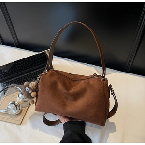 Detail of a brown suede pillow bag with a plush doll charm and a wide handle grip