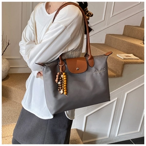 Détail du sac cabas en nylon gris avec anses en cuir et breloque en bois sur l'épaule