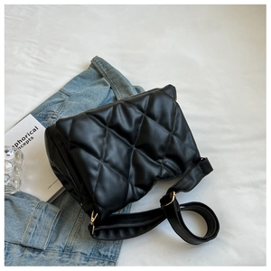 Detail view of the black quilted crossbody bag with golden metal buckles on a styled setup