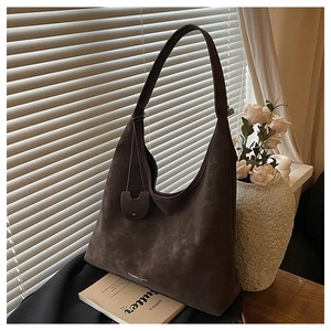 Détail du sac cabas en daim marron foncé avec bandoulière intégrée et petit pendentif