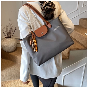 Détail du sac cabas en nylon gris avec anses en cuir marron et logo de la marque