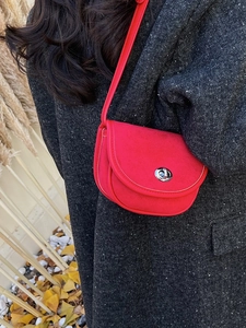 Minimalist red suede saddle bag with silver clasp worn on a grey winter wool coat