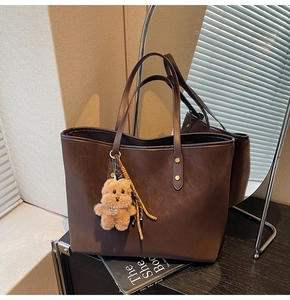 Detail einer dunkelbraunen Shopper-Tasche mit Plüsch-Hundeanhänger auf Holzoberfläche