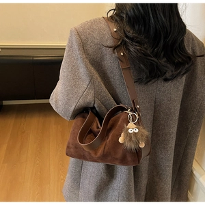 Detail of dark brown suede crossbody bag with fluffy monster charm and rivet strap