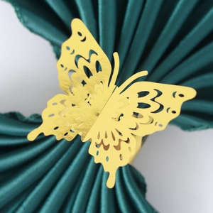 Golden hollow butterfly napkin ring with laser-cut design on green fabric background