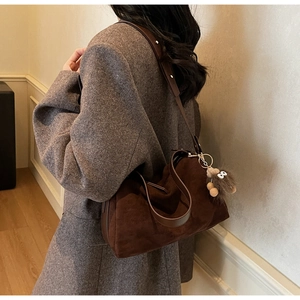 Detail of a brown matte suede shoulder bag with a plush monster charm on a model