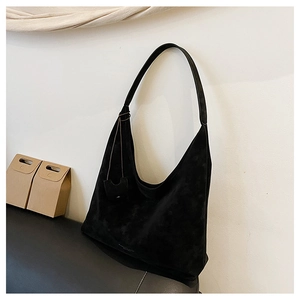 Détail d'un sac hobo en daim noir avec pendentif assorti posé contre un mur blanc