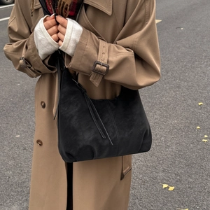 Detail shot of black hobo bag with vintage tassels and soft suede texture on trench coat