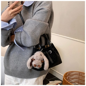 Detail showing black suede bucket bag with leather strap and grey plush bunny charm