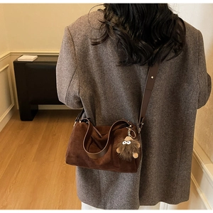 Detail of dark brown faux suede pillow bag with plush monster charm and leather straps