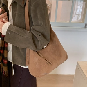 Detailed view of the brown suede hobo bag worn with a green jacket and plaid scarf