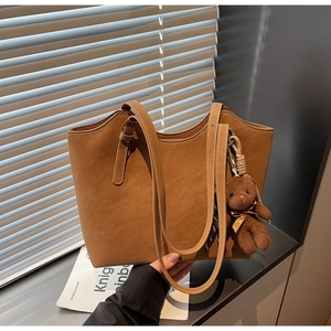 Détail d'un sac cabas en cuir marron avec un petit ours en peluche et logo embossé précis