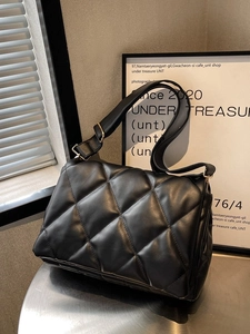 Quilted black hobo tote bag with wide strap and gold hardware on a minimalist stage
