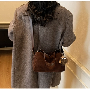 Detail of a brown suede pillow bag with a plush eye charm on a grey winter coat