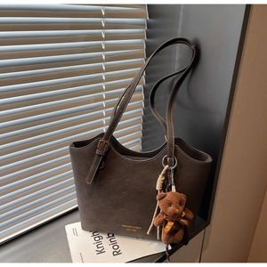Détail d'un cabas marron foncé avec logo doré et charm d'ours en peluche avec ruban d'amour