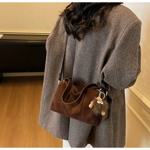 Detail of dark brown suede cylindrical crossbody bag with cute plush monster charm