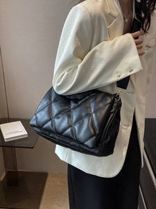 Quilted black leather tote bag with wide strap and gold hardware worn by model