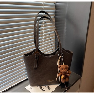 Détail du cabas mat marron foncé avec fines bretelles et pendentif ours sur un rebord