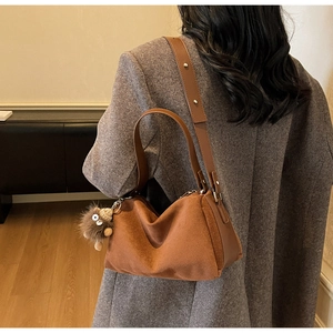 Brown suede shoulder bag with plush charm accessory shown in a cozy indoor setting