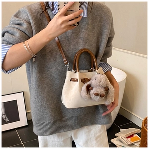Detail of cream bucket bag with brown handle, featuring a plush bunny charm on a model