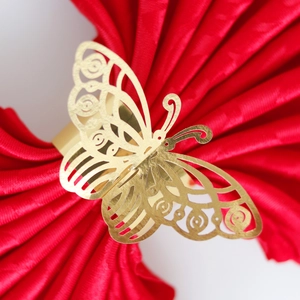 Macro shot of gold butterfly napkin ring with laser-cut hollow details on red satin fabric