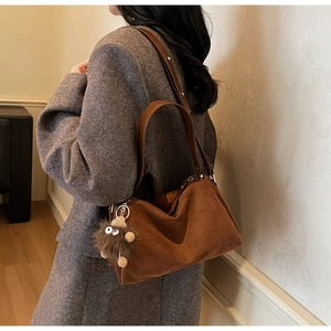 Detail of dark brown suede handbag with leather strap and plush monster charm
