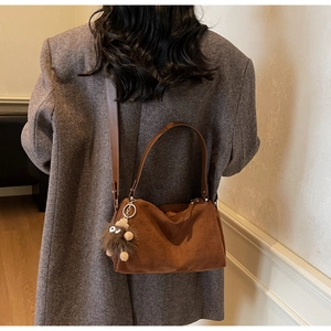 Detail of brown suede tote bag featuring a cute fuzzy monster charm on a wool coat