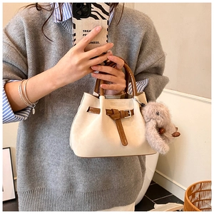 Detail of beige pleated handbag with brown handles and a plush rabbit charm accessory
