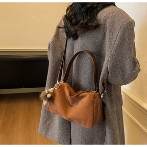 Detailed texture of brown faux suede shoulder bag with plush bear charm on grey coat