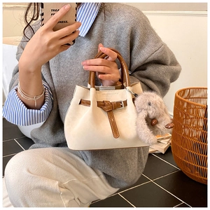 Detailed view of beige suede bucket bag with brown leather handle and plush rabbit charm