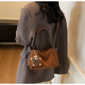 Close-up of dark brown suede shoulder bag featuring a cute furry monster charm accessory