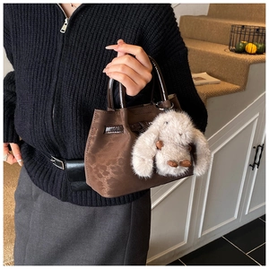 Detail of dark brown embossed handbag with glossy handle and plush rabbit charm