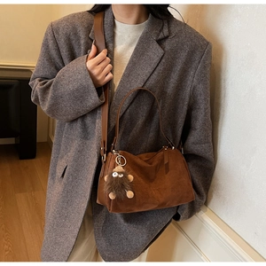 Brown suede shoulder bag detail featuring a cute plush monster charm and leather strap