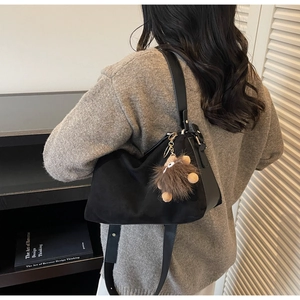Detail of black suede and leather crossbody bag with a brown plush monster charm on handle