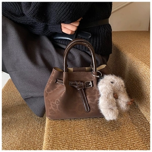 Close-up of deep brown bucket bag with metallic buckle and cute plush rabbit charm