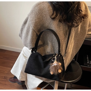 Detail of black matte pillow shoulder bag with a cute plush monster charm accessory