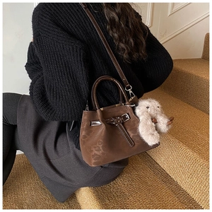 Brown vintage bucket bag shown with detachable strap and cute plush rabbit charm